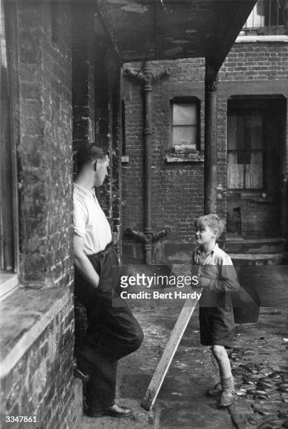 Albert Lilley, a blacksmith's striker, chatting to young Dennis Smith at Hermitage in Wapping, London, where they both live. Original Publication:...