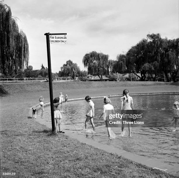 White children paddling in a pond marked by a sign reading 'For European Children Only'.