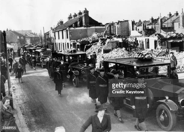 Funeral cars drive slowly through a bomb-damaged street in Portsmouth, accompanied by an escort of British soldiers and sailors. Twenty-five victims...