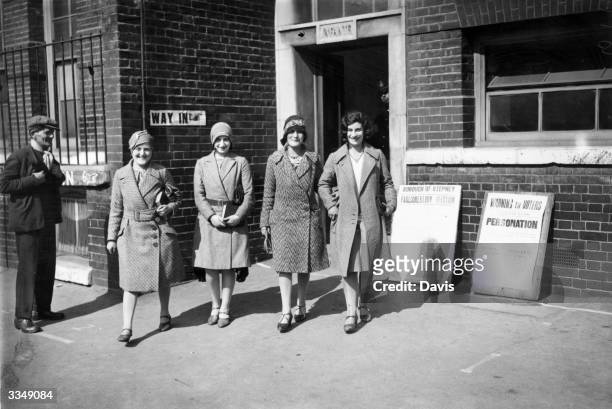 Four young women wearing the cloche hats typical of the 'flapper' era leave the polling station of the London Borough of Stepney, after voting in the...