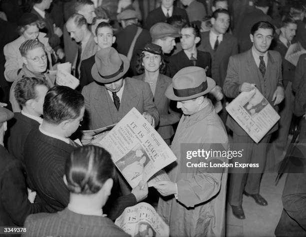 People reading copies of The Daily Express newspaper after the Munich agreement. The headline reads 'It Is Peace'.