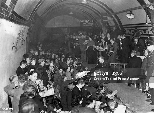 Man handing out information to the members of the audience during a concert given by ENSA at Aldwych underground station, London. The audience is...