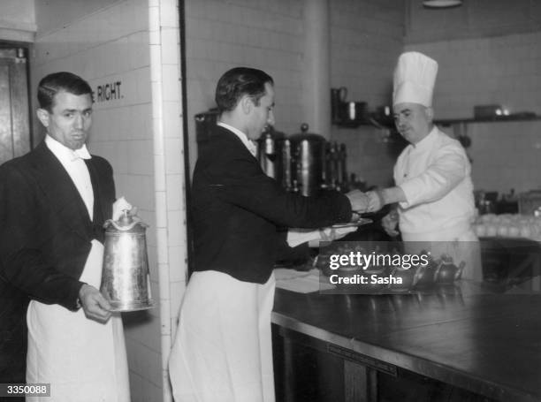 Waiters collecting hot beverages from a chef in the kitchen at the Savoy Hotel, London.