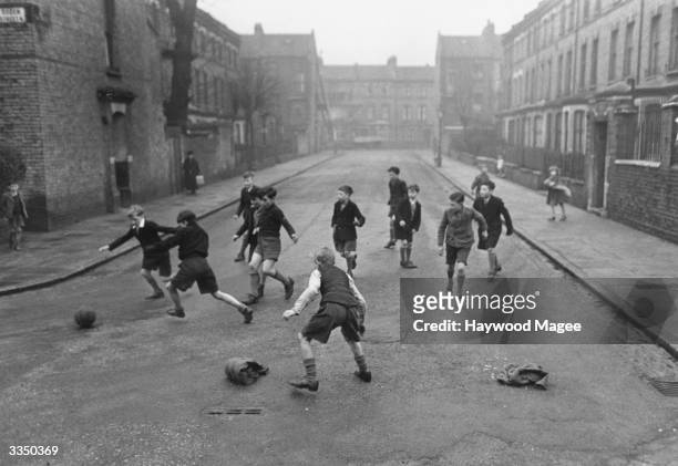 Boys playing football in a residential street in London. Original Publication: Picture Post - 5005 - Children's Street Games - pub. 1950
