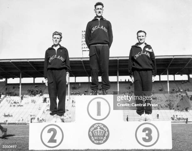 English professional athletes Frank Sando, Peter Driver and Jim Peters on the rostrum at the British Empire Games, Vancouver, Canada after winning...