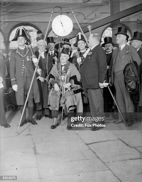 The new Mayor of High Wycombe being weighed as part of a traditional inauguration ceremony. He is surrounded by traditionally dressed officials.