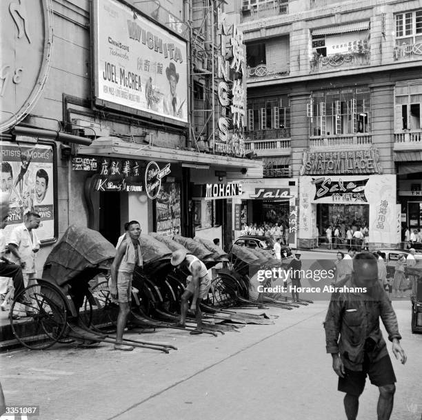 Line of rickshaws parked outside a cinema in Hong Kong, awaiting a fare. The rickshaw is still a popular mode of transport, as it is unaffected by...