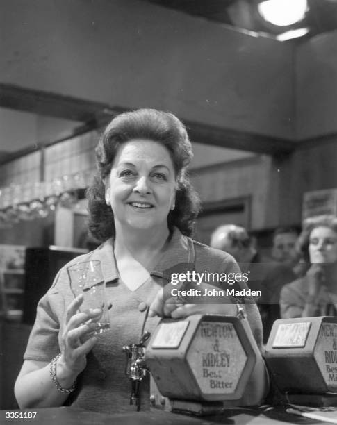 Actress Betty Driver as barmaid Betty Turpin, serving behind the bar at the Rover's Return pub in the television soap opera 'Coronation Street'.