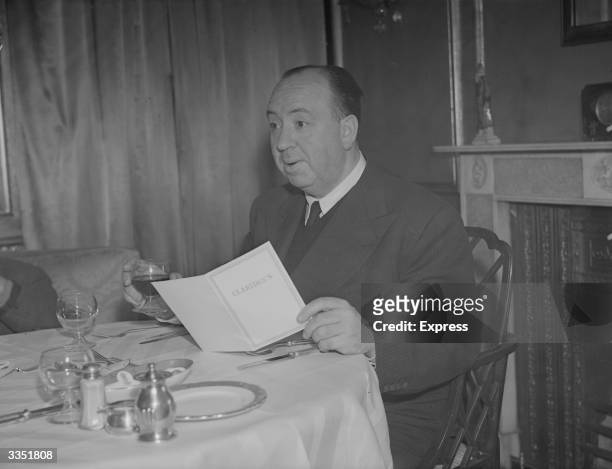 British born film director and producer Alfred Hitchcock , drinking a glass of wine as he reads the menu at Claridges in London.