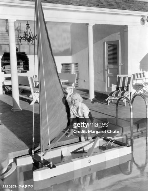 Star Jean Harlow about to embark on a short 'cruise' round her swimming pool in a balsa sail boat.