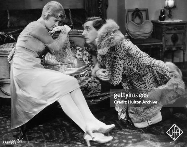 American comic actor Edward Everett Horton , wearing a leopardskin fur coat, kneels to speak intimately with actress Laura La Plante, in a scene from...