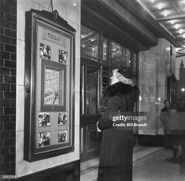 Alice, a barmaid from Bermondsey, uses her day off to go to the cinema, London, 1939. She is looking at a poster for Norman Z. McLeod’s romantic...