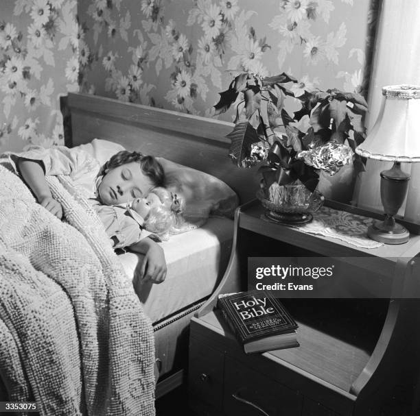 Little girl sleeps peacefully in bed her doll by her side. A bible rests on her bedside table.