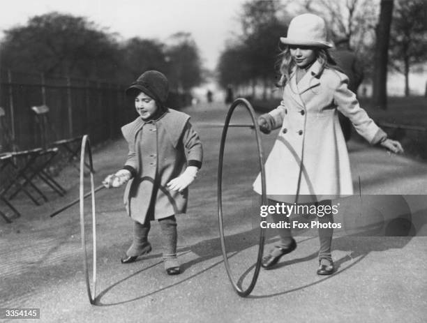 Two girls rolling hoops with sticks in Hyde park in London.