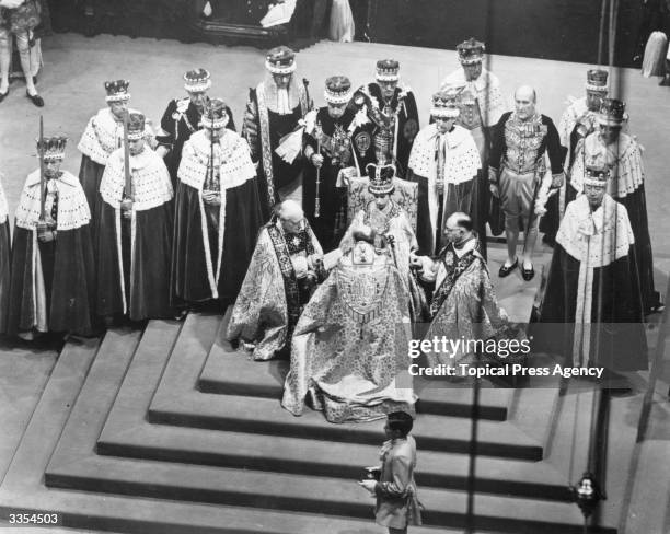 Queen Elizabeth II seated on a throne in Westminster Abbey attended by dignitaries whilst Bishops pay homage to her.