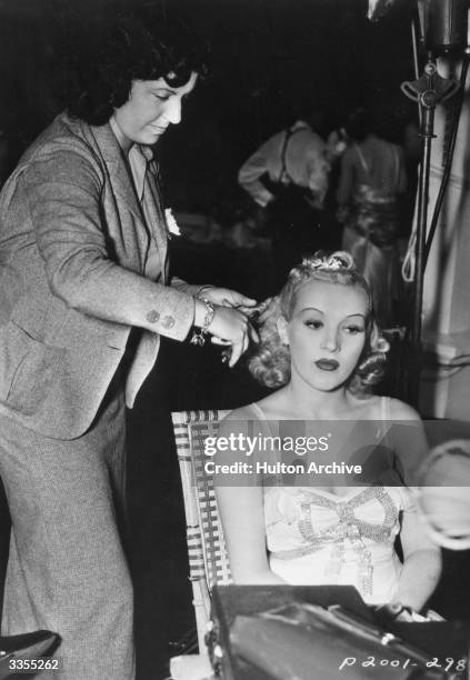 American actress Betty Grable having her hair done on the set of her latest film 'College Swing' , directed by Raoul Walsh for Paramount.