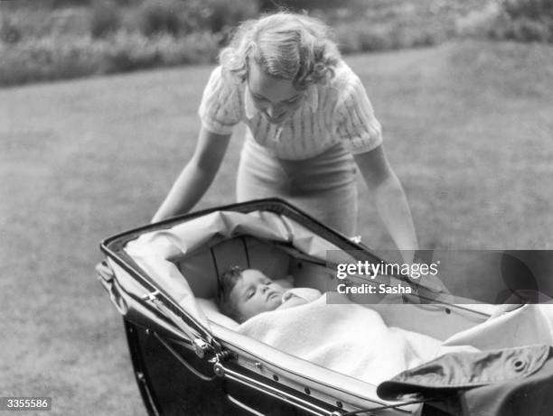 Actress Diana Beaumont leaning over her baby son who is asleep in his pram.