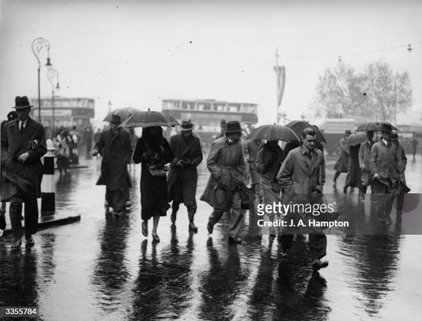 People wearing raincoats and sheltering under umbrellas cross a road at Blackfriars, London, in the rain.