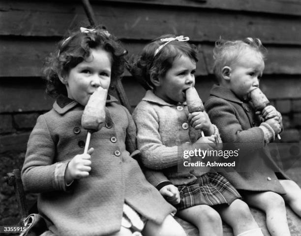 Three young children enjoying a portable, healthy snack - a carrot on a stick. Ice cream is not available due to war rationing.