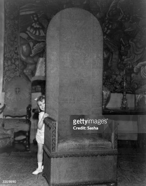 Peering round a large high backed tapestry covered chair in her mother's London home is Patricia, young daughter of American actress Bessie Love who...