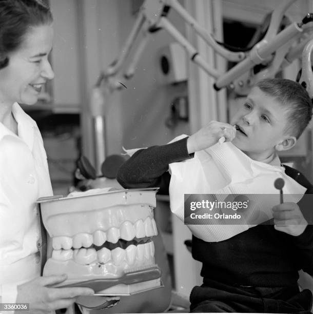 Dental technician uses a giant model of a set of dentures to explain proper brushing techniques to a young patient.