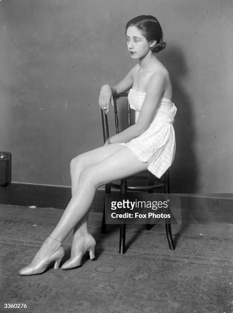 Girl in high heels and a short sun-dress sits on a chair, smoking.