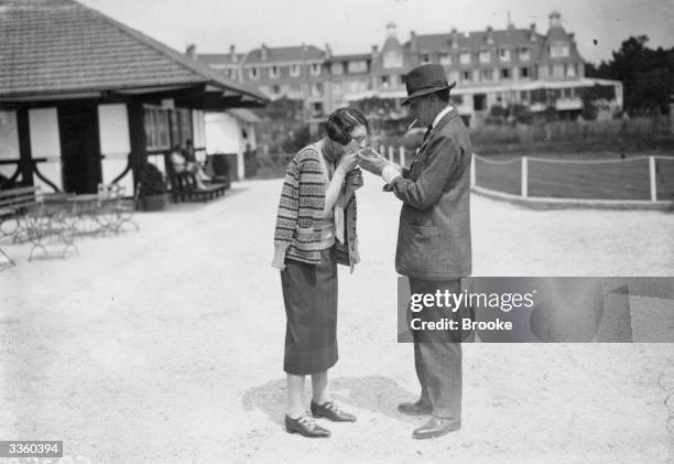 Mr Charles Wilmot lights a cigarette for Mrs Kenneth MIlls at Le Touquet, in France. A holiday destination proving popular amogst fashionable English...