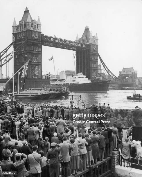 Crowds watching the Royal Yacht Britannia, with the Queen and Duke of Edinburgh aboard, as it passes under Tower Bridge on its way to Westminster,...