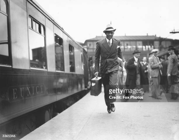 Snappily dressed Jesse Owens makes a dash for a train at London's Waterloo station. He will be joining the liner 'Queen Mary' en route for New York.