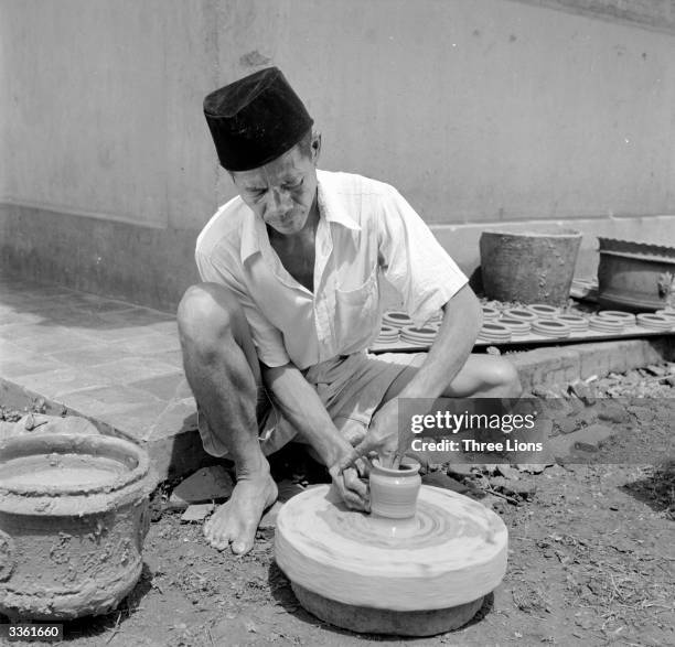 Potter forms a jar at his wheel in the yard of his home in Java, Indonesia.