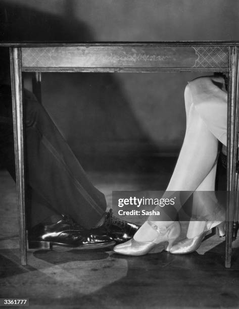 Two pairs of feet, one male, one female, meet underneath the table.