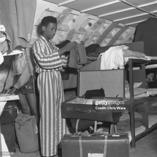 Seventeen year-old Jamaican settler, Rudolph 'Nick' Collins , folding his clothes at a temporary reception centre in a converted air-raid shelter...