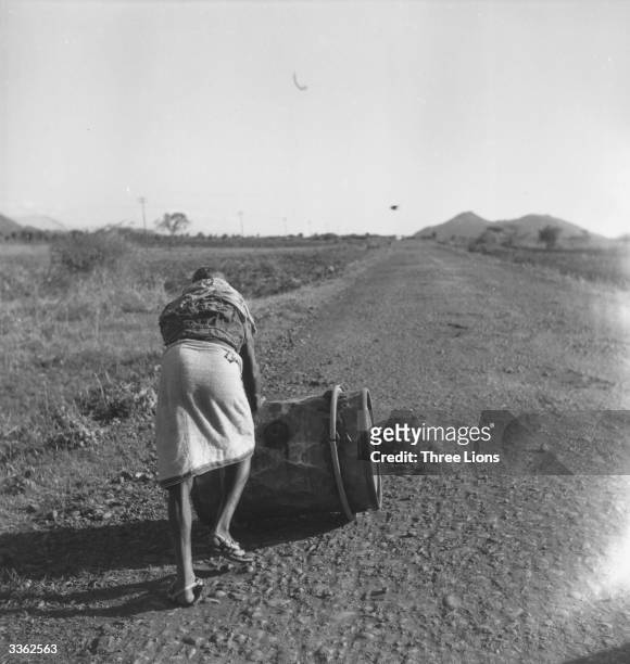 Man pushes a barrel of water along the road towards his village. The lack of water along sections of the Strada, Ethiopia, necessitates rolling it...