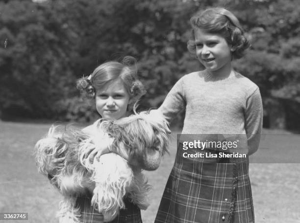 Queen Elizabeth II and her younger sister Princess Margaret in the grounds of the Royal Lodge, Windsor. Princess Margaret is holding one of their pet...