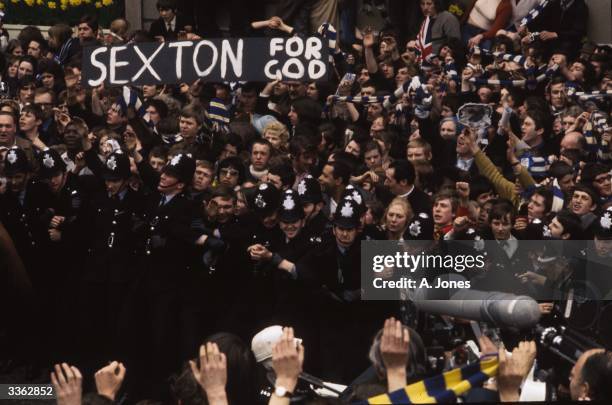 Police keeping back crowds of Chelsea Football Club supporters as they strain for a glimpse of manager Dave Sexton. A banner in the crowd reads...