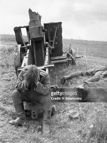 German soldier sitting with his head in his hands by a destroyed heavy artillery gun and the corpse of one of his compatriots during the Kursk battle...