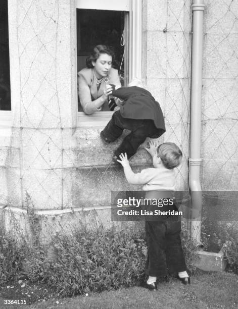Queen Elizabeth II and Charles, Prince of Wales helping Princess Anne through an open window at Balmoral Castle, Scotland.