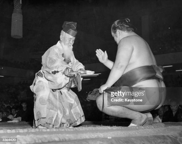 Sumo wrestler is presented with his prize money wrapped in rice paper and ribbons, by Inosuke Shikimori.