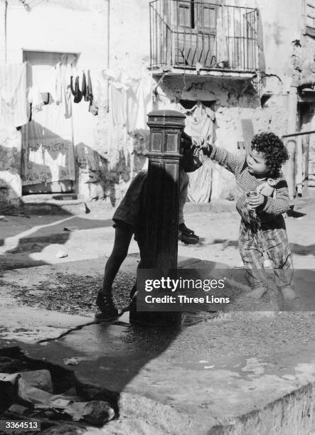 Young child at a water fountain in a slum courtyard in Italy. Three taps have to supply about 260 families and waste water runs through open trenches...