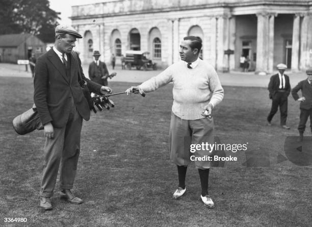 Golfer Walter Hagen takes a club from his giant caddie J W Williams who is 6ft 2'' tall during practice for the round against Archie Compston at...