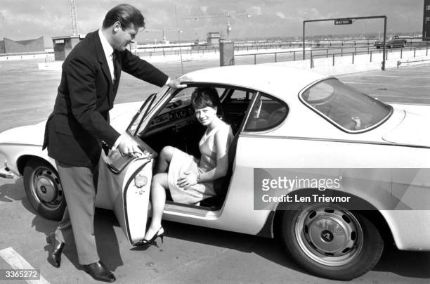 English film actor Roger Moore opening the door of his Volvo for Isabelle McMillan in a scene from the television series 'The Saint'.