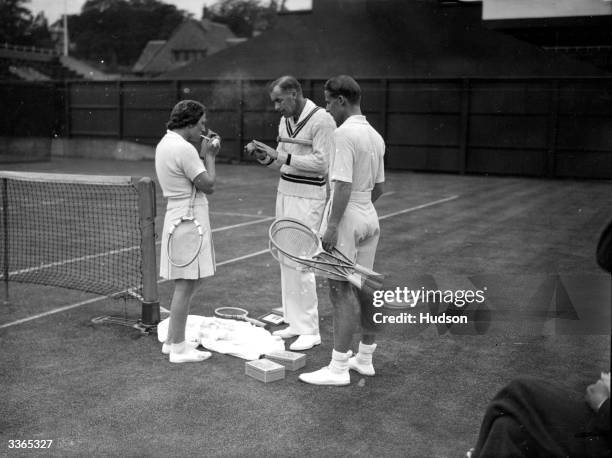 American tennis player Helen Jacobs lights a cigarette while fellow American Bill Tilden toys with the ball and Bunny Austin of Britain looks on. The...