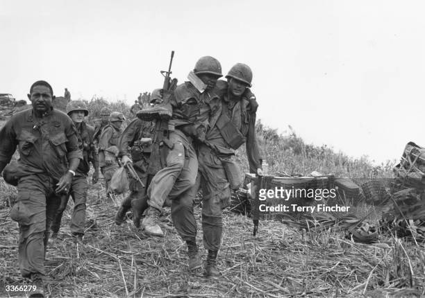 Soldiers, one wounded and being carried by a colleague, walking down Hill Timothy, during the conflict in Vietnam.