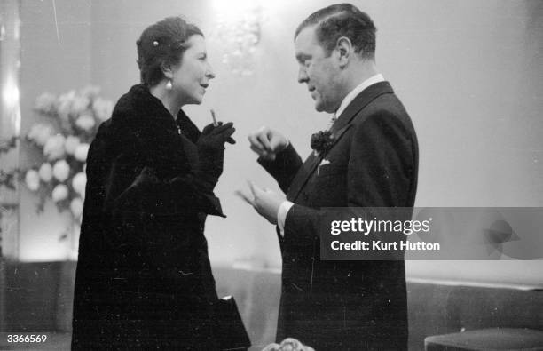 English couturier and court dressmaker Sir Norman Hartnell in conversation with the wife of the French ambassador in London. Original Publication:...