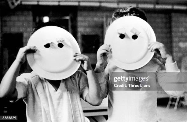 Two children holding up paper plate masks with holes for eyes.