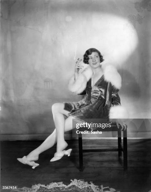 Actress Margaret Campbell, wearing a fur-trimmed outfit with matching slippers, smoking a cigarette.