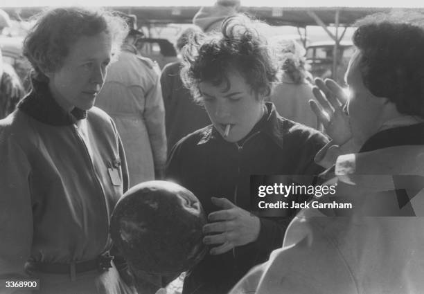 Raing driver Pat Moss, winner of the first ever Ladies Invitation race at Goodwood, examining the helmet of a competitor whose car was overturned...