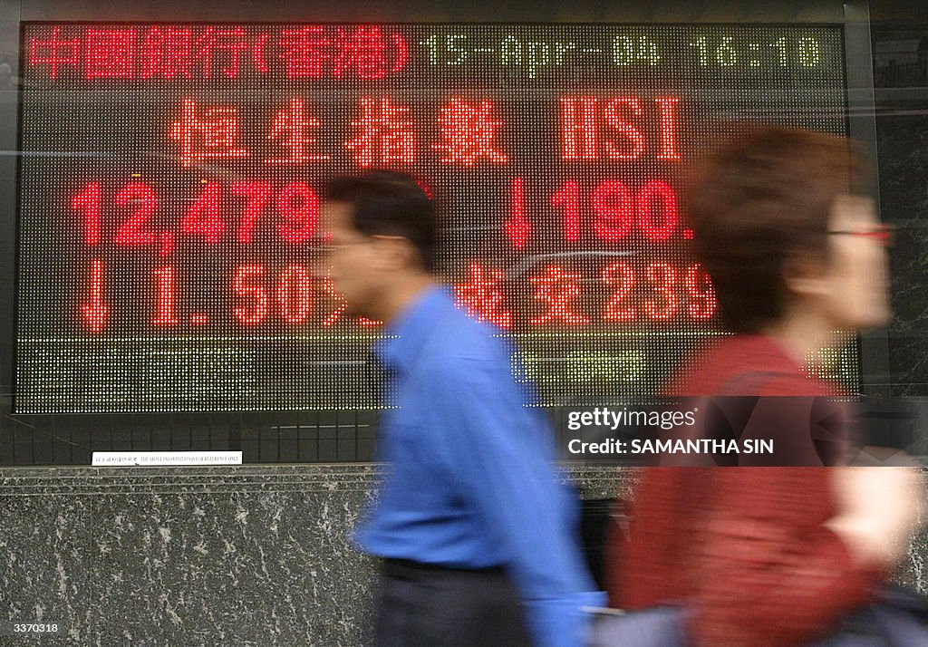 Pedestrians walk past a sign board showi