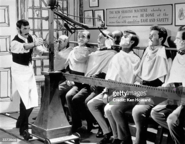 English comedian Eric Sykes reviving the 'mass shaving machine', a nineteenth century invention, which can shave a dozen men at the same time, on an...