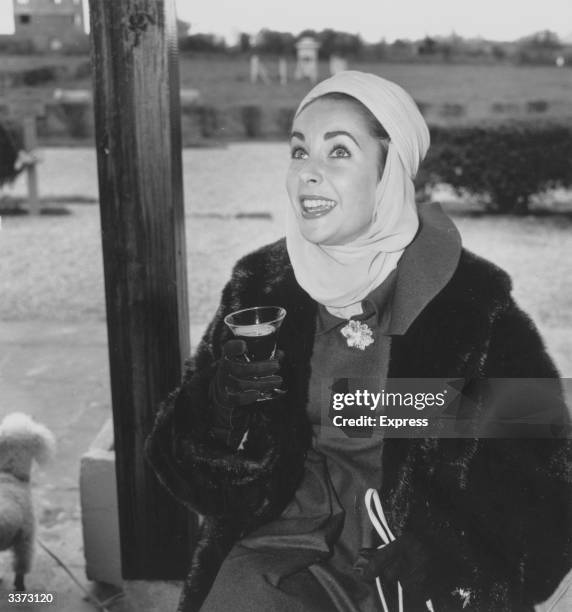 British-born US actress Elizabeth Taylor wearing a turban and drinking a glass of wine.